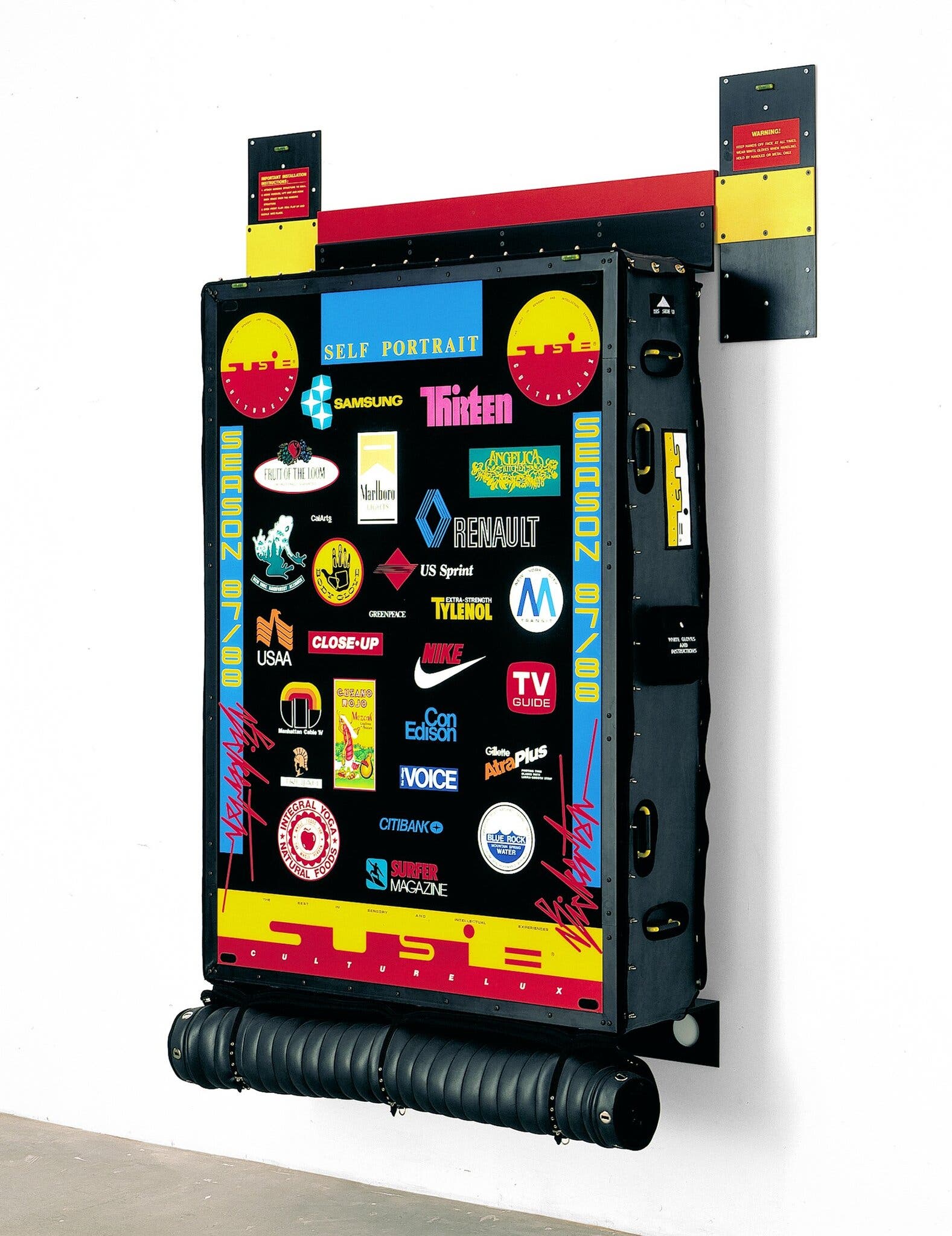 “Tormented Self-Portrait (Susie at Arles) #2,” 1988. His Susie logo floats amid a sea of corporate logos. Aligned with the Neo-Geo movement of the late-1980s, Bickerton made ironic constructions suggesting a new personal identity for living in a consumer society.Credit...Ashley Bickerton, via Gagosian